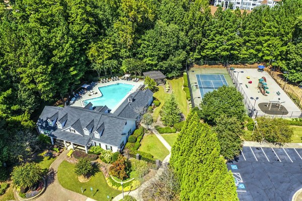 Aerial view of luxury apartments featuring a pool, tennis court, and playground in a lush green community