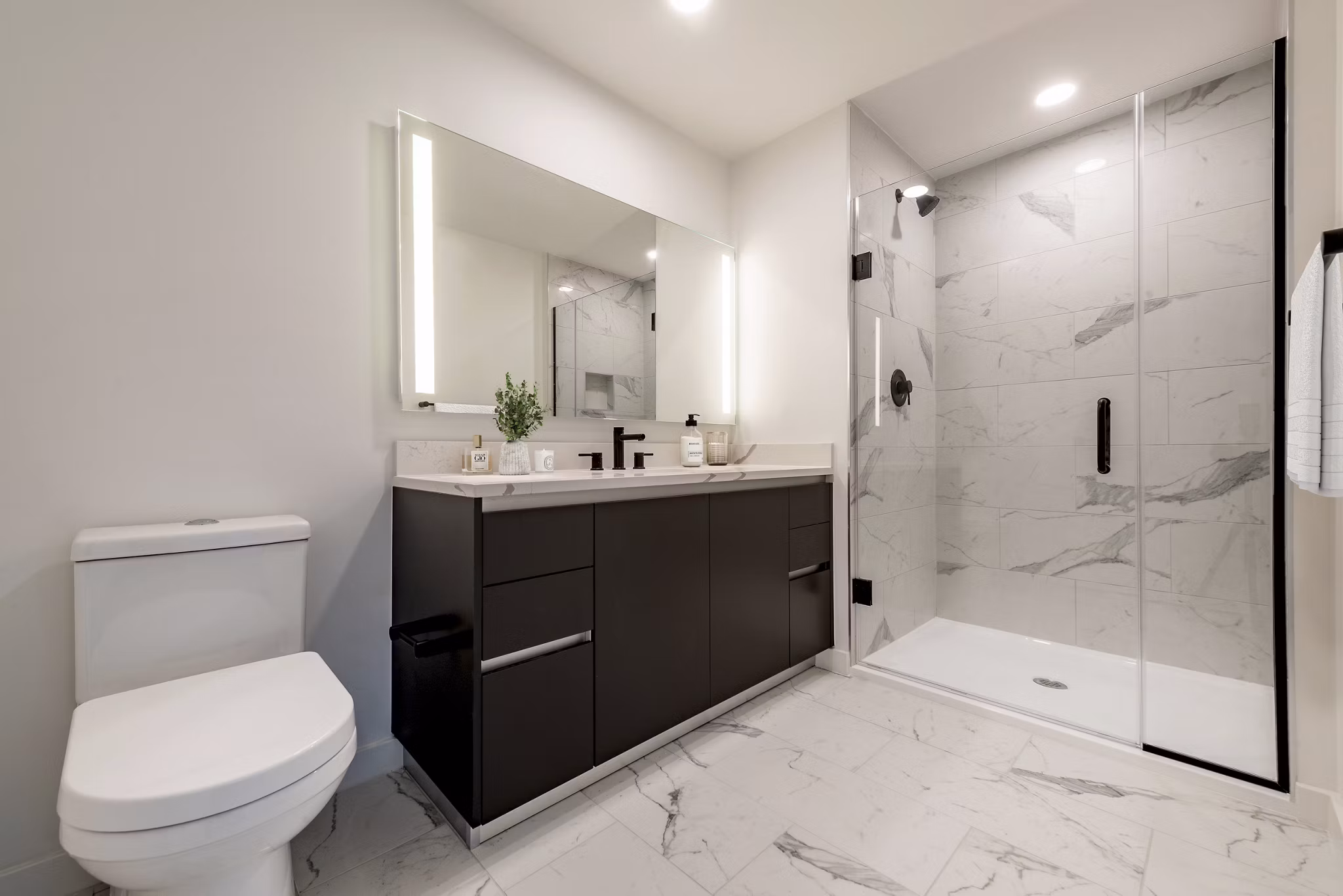 Modern bathroom featuring a sleek vanity, large mirror, and glass-enclosed shower in luxury apartment