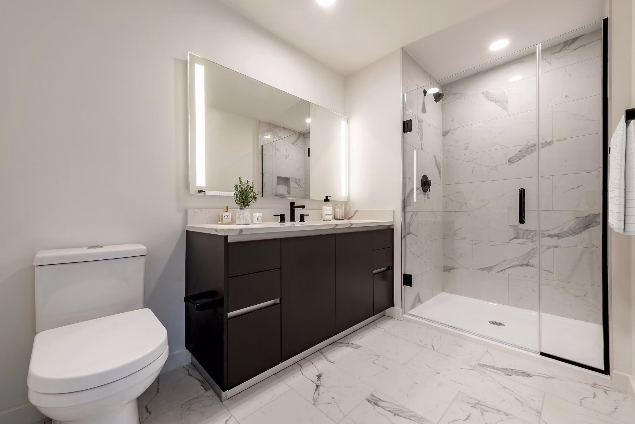 Modern bathroom featuring a sleek vanity, large mirror, and glass-enclosed shower in luxury apartment