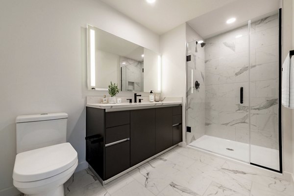 Modern bathroom featuring a sleek vanity, large mirror, and glass-enclosed shower in luxury apartment
