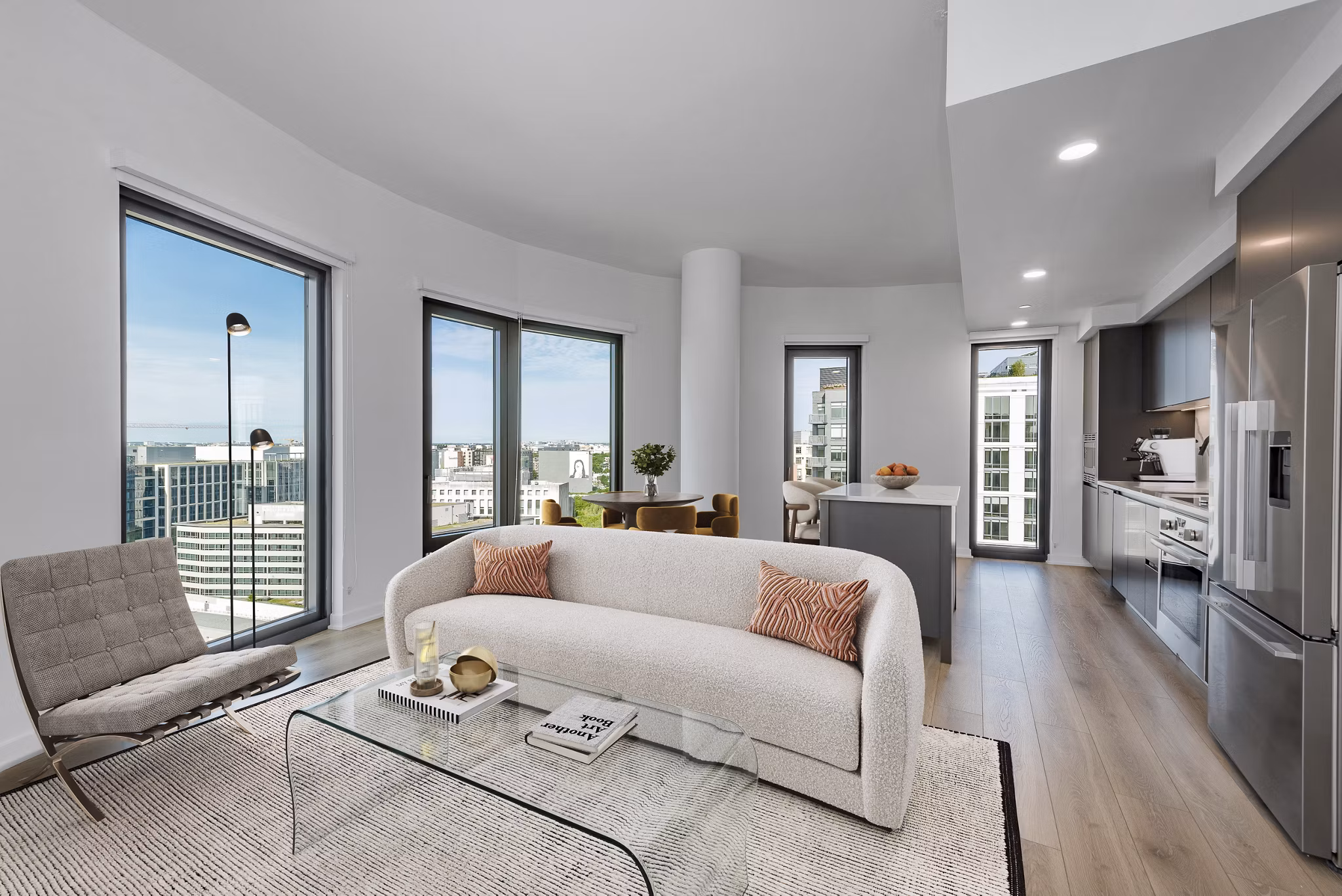 Modern living room and kitchen with city views, sofa, glass coffee table, and stainless steel appliances in luxury apartment