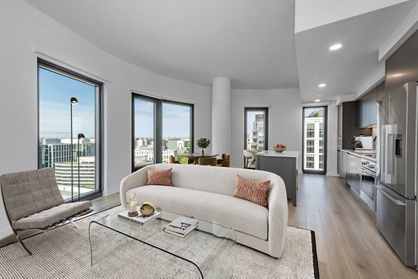 Modern living room and kitchen with city views, sofa, glass coffee table, and stainless steel appliances in luxury apartment