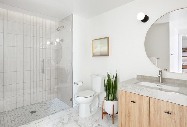 Modern bathroom with marble countertops and large mirror at Jardine Apartments, by Greystar