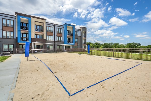 Beach volleyball court surrounded by lush greenery at The Holston Apartments, offering recreational fun and sports amenities for residents