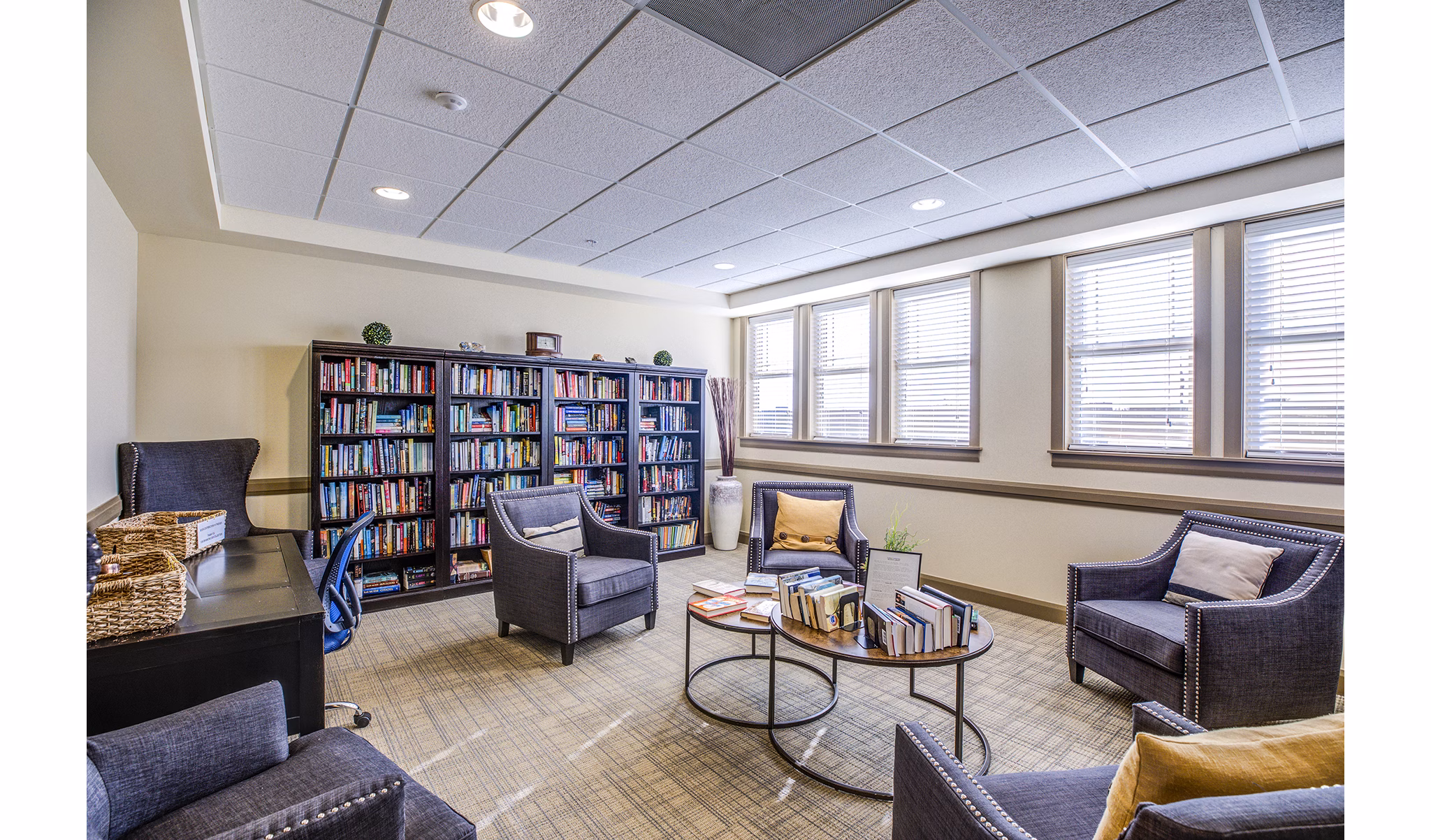 Everleigh Central Park Apartments: Cozy clubhouse library with plush seating and wooden bookshelves, perfect for reading and relaxation