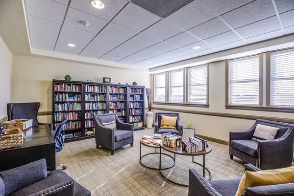 Everleigh Central Park Apartments: Cozy clubhouse library with plush seating and wooden bookshelves, perfect for reading and relaxation
