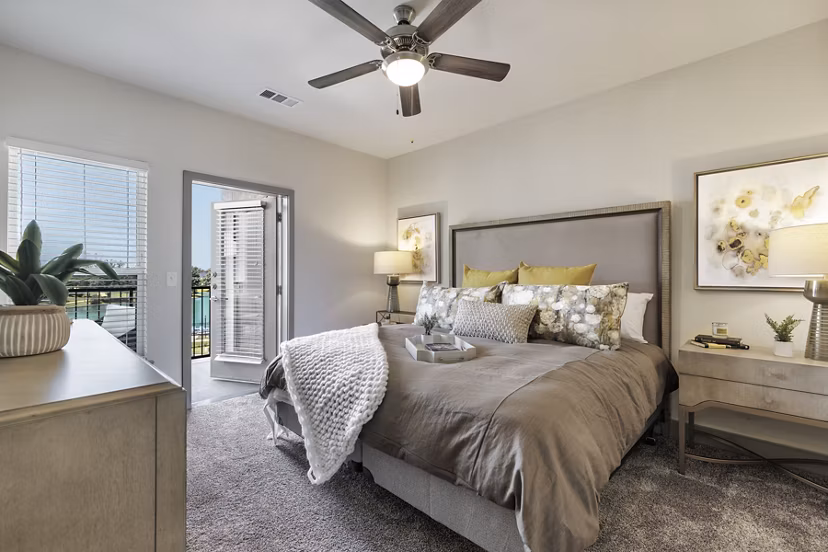 Cozy bedroom with neutral tones and large windows in Arista Riverstone Apartments
