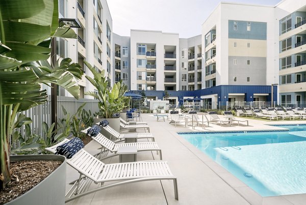 Modern outdoor pool area at Parallel Apartments, featuring sun loungers and lush landscaping, offering luxury amenities for residents