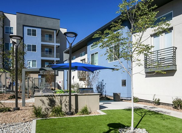 Modern luxury apartment complex with landscaped outdoor seating and blue umbrellas in the courtyard