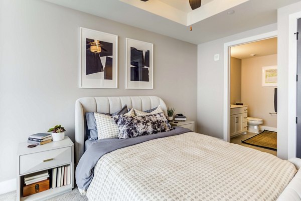 Elegant bedroom with modern decor at The Bower Apartments, featuring cozy queen bed and large windows for natural light