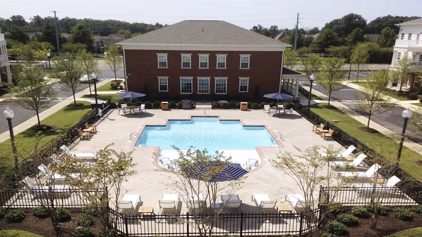 Sunlit outdoor pool at Carrington at Schilling Farms Apartments with lounge seating and lush landscaping
