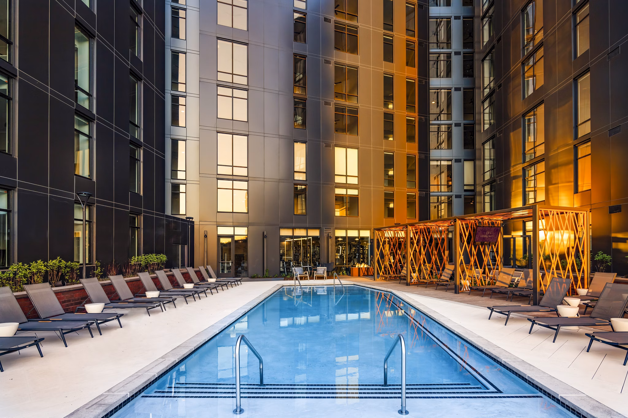 Luxurious pool at Harlowe Apartments with sun loungers and modern landscaping, perfect for relaxation and leisure activities