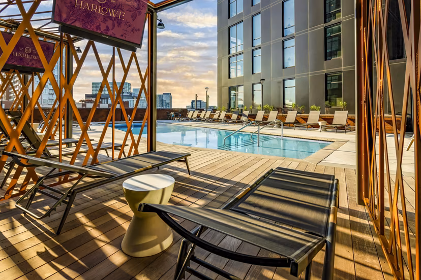 Harlowe Apartments: Luxurious pool patio with stylish loungers and greenery, perfect for relaxing and socializing outdoors