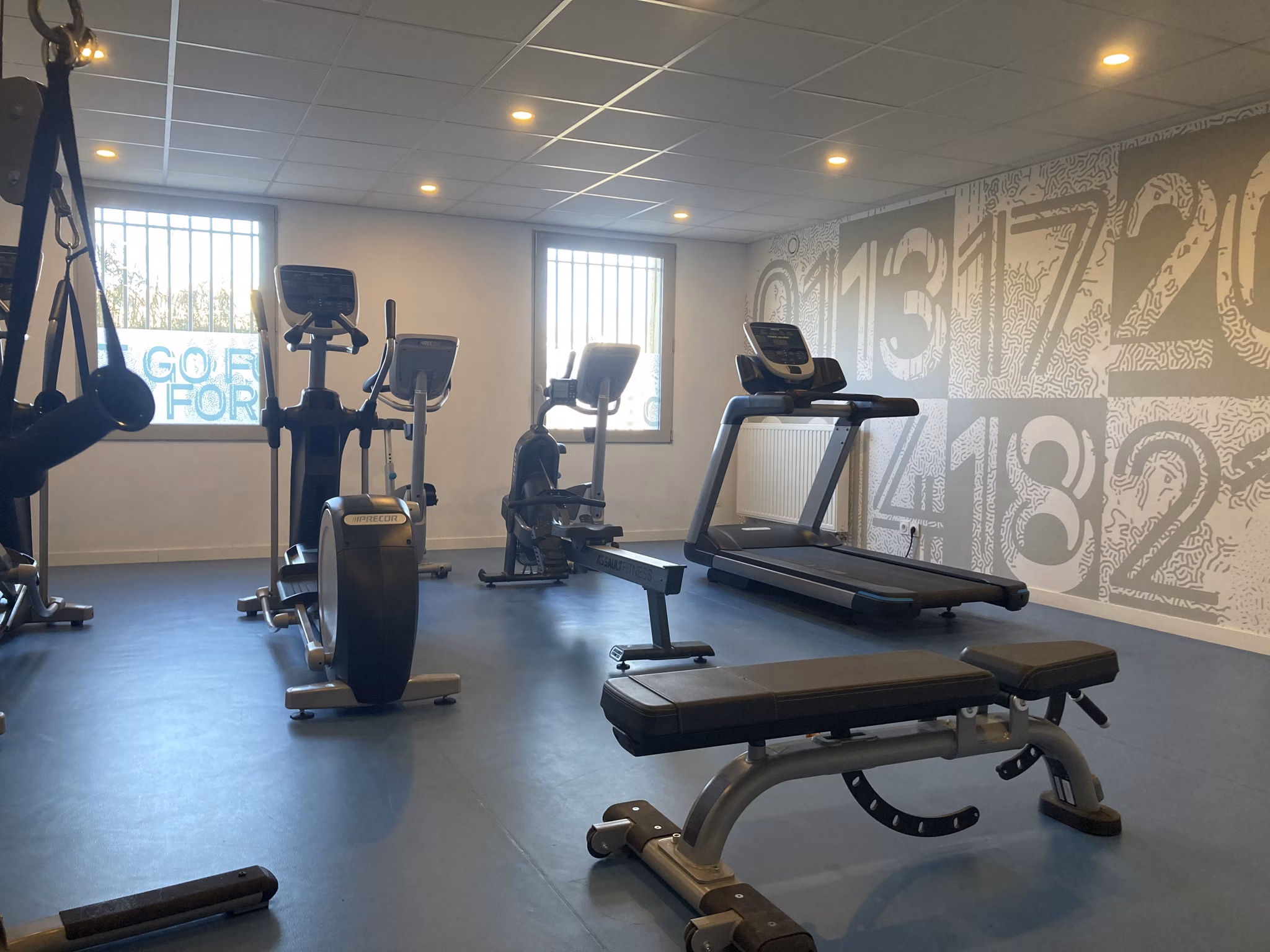 Fitness room featuring treadmills, a variety of weights, and gym equipment set against a large window for natural light.