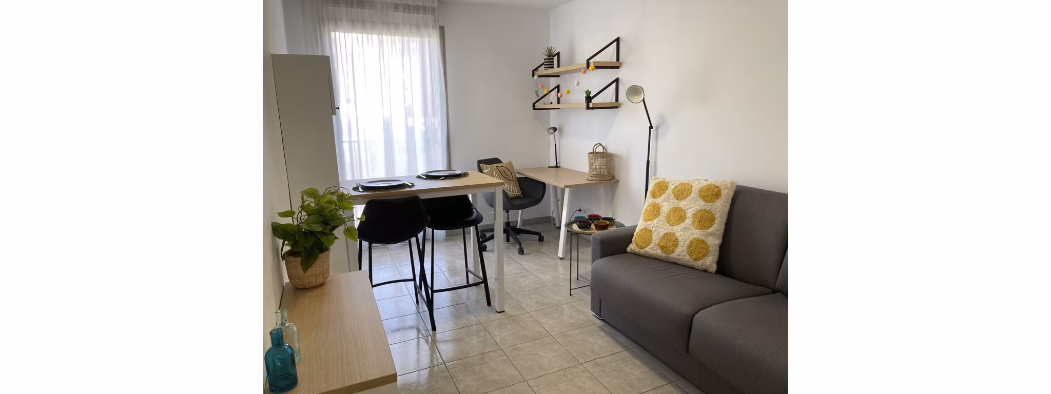 Minimalist living space with a comfortable sofa, decorative cushions, and modern furniture set against a neutral backdrop.