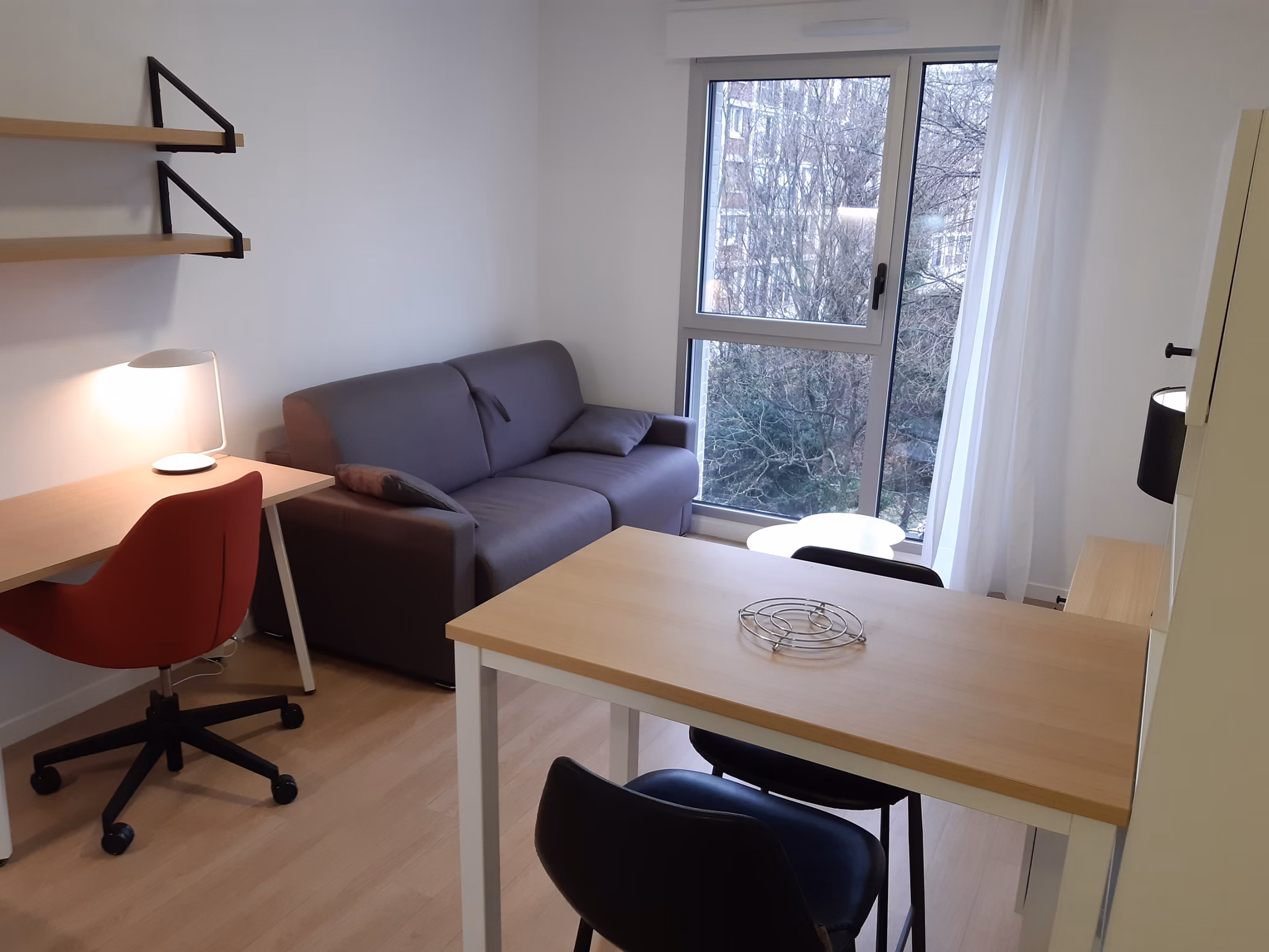 Comfortable living space with a gray sofa, workspace, and large window providing natural light and a homey feel.
