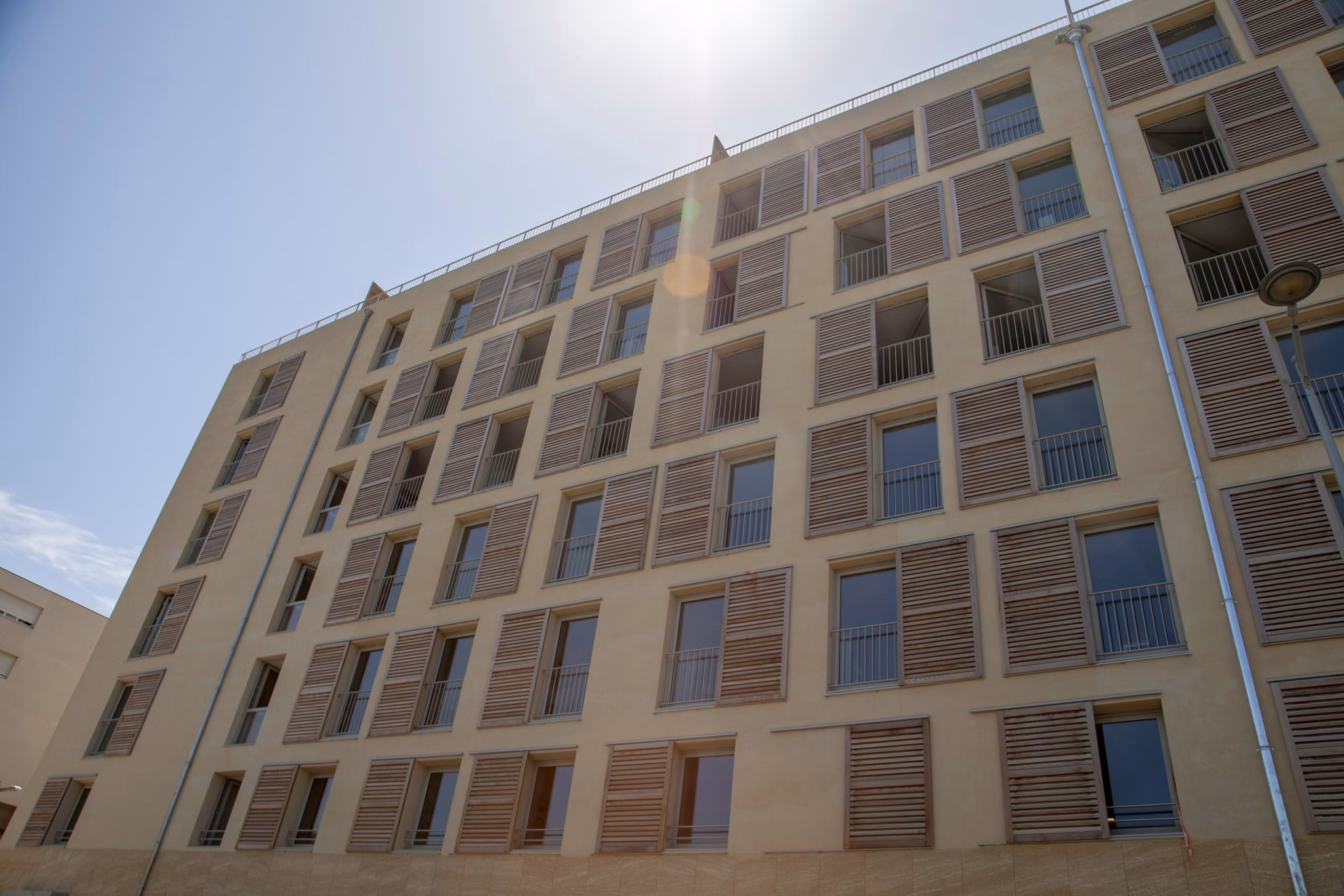 Wide-angle shot of a contemporary building facade with brickwork and spacious windows, surrounded by other urban structures.