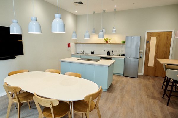 Modern communal kitchen and dining area at Canvas Wembley apartments, featuring light wood furniture, pendant lighting, and contemporary appliances.