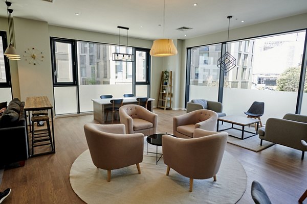 Bright and spacious living room area at Canvas Wembley apartments, featuring modern furniture, large windows, and wooden flooring.