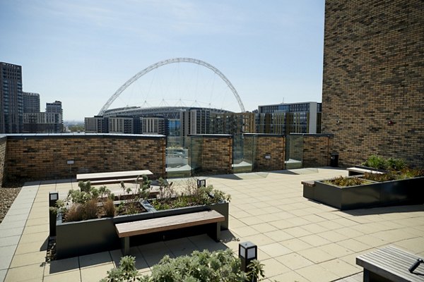Spacious public patio area at Canvas Wembley apartments, featuring seating, planters with greenery, and a view of the iconic Wembley Stadium arch in the background.