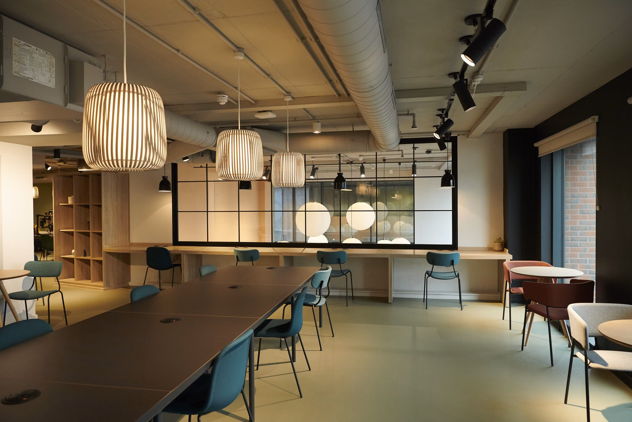 Modern common area at Canvas Coventry Arundel House in Coventry, featuring a long table, colorful chairs, stylish pendant lights, and industrial-style interior design.