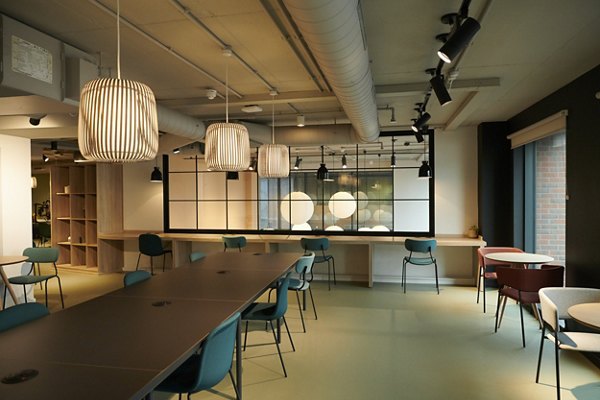 Modern common area at Canvas Coventry Arundel House in Coventry, featuring a long table, colorful chairs, stylish pendant lights, and industrial-style interior design.