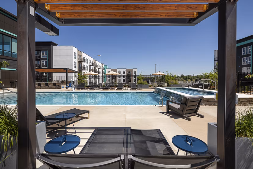 Luxury pool with lounge chairs and lush landscaping at Revel Apartments, ideal for relaxation and leisure