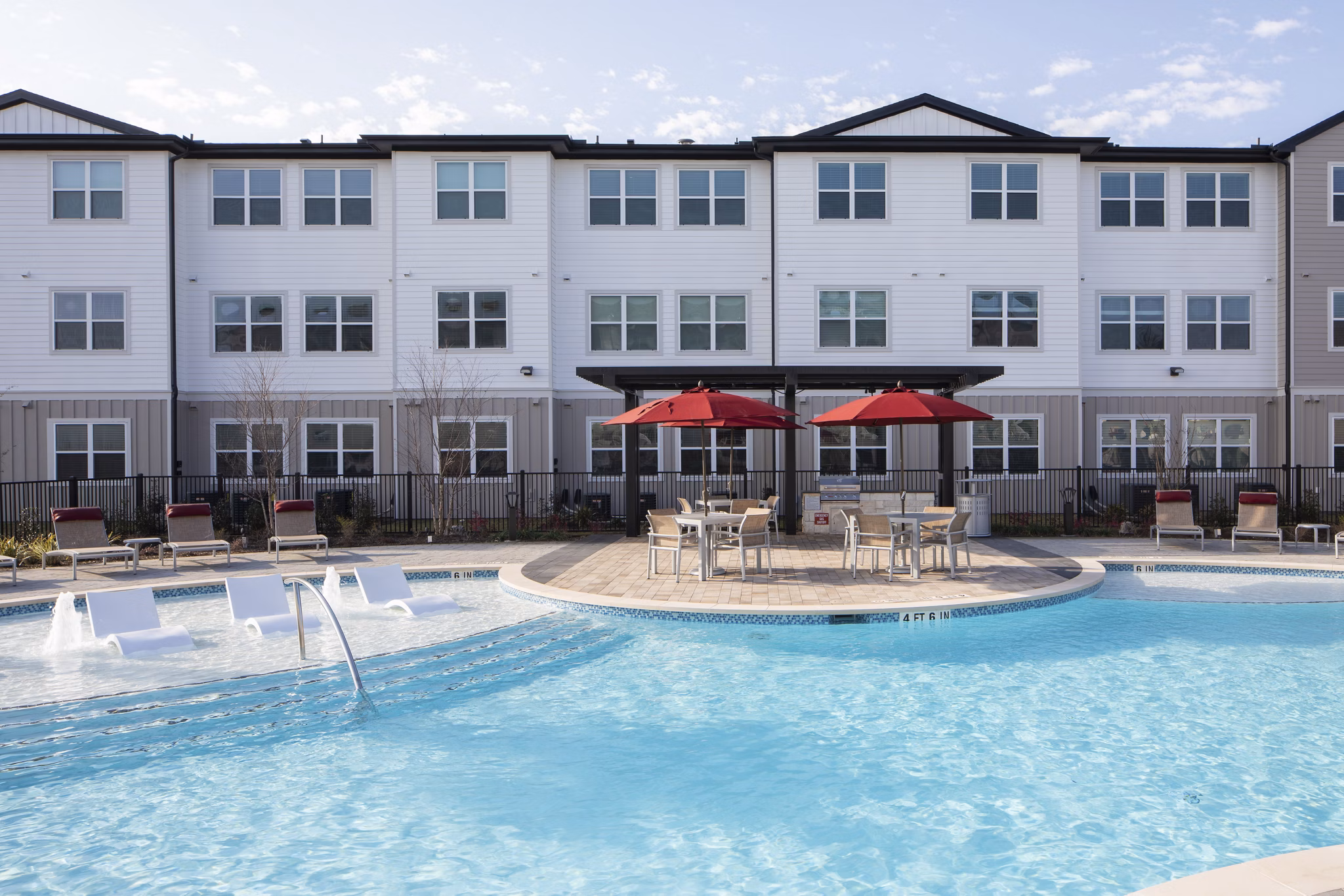 Luxury apartment building with a swimming pool and lounge chairs under red umbrellas in a serene outdoor space