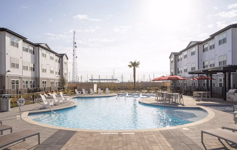 Outdoor swimming pool area with lounge chairs and umbrellas near luxury apartments