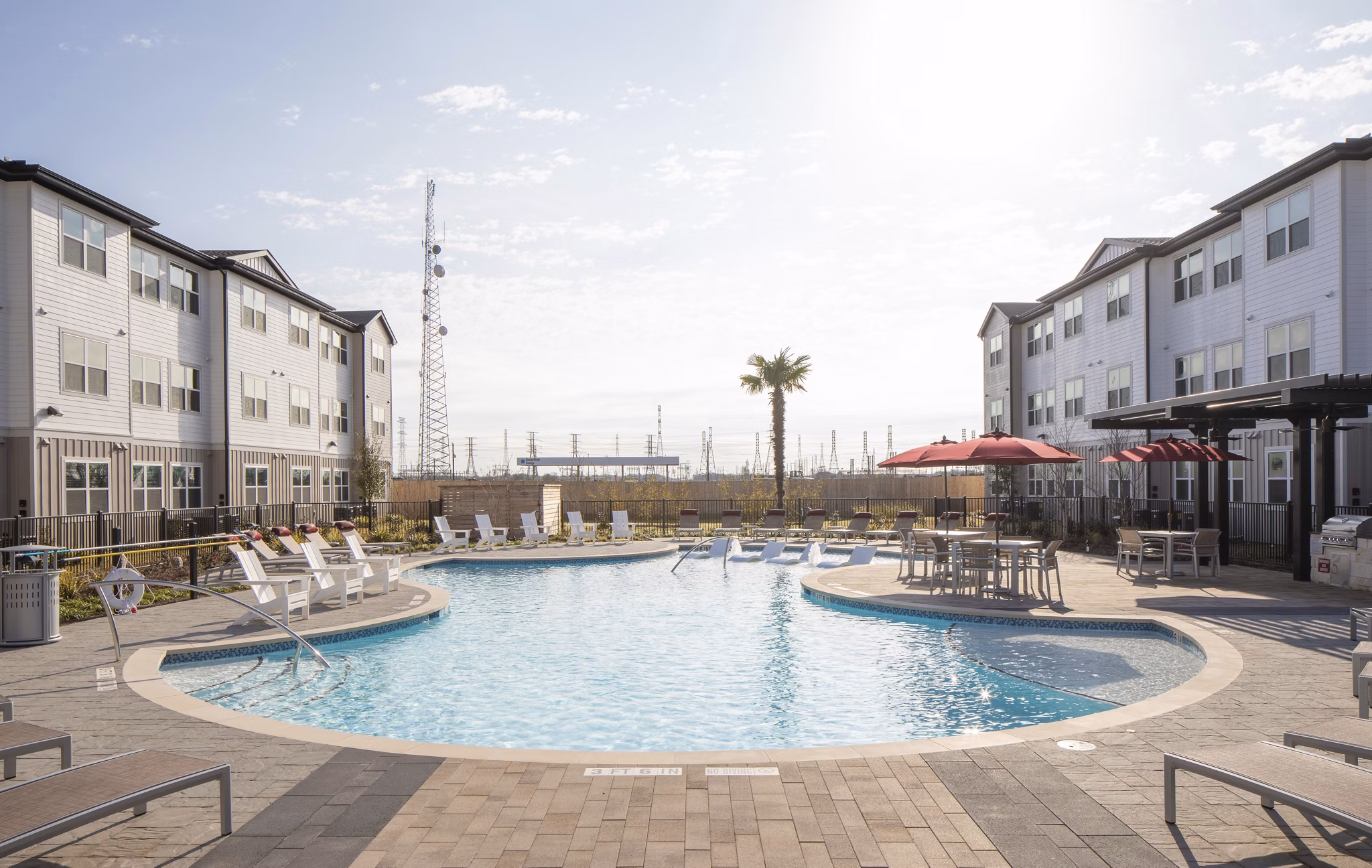 Outdoor swimming pool area with lounge chairs and umbrellas near luxury apartments