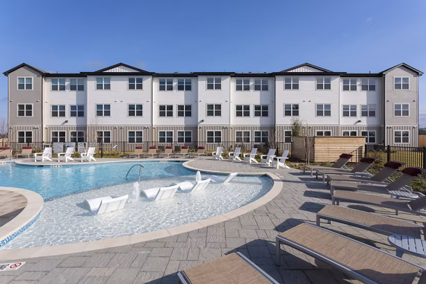 Luxury apartment building with a swimming pool and lounge chairs in the foreground