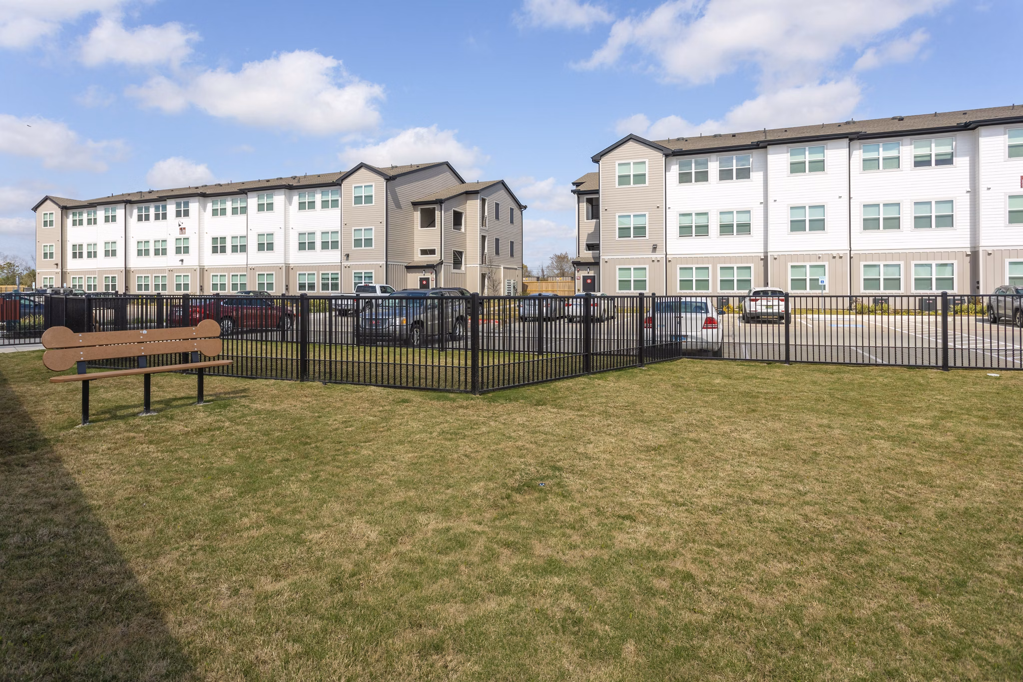 Grassy area with a bench and fenced section surrounded by luxury apartments
