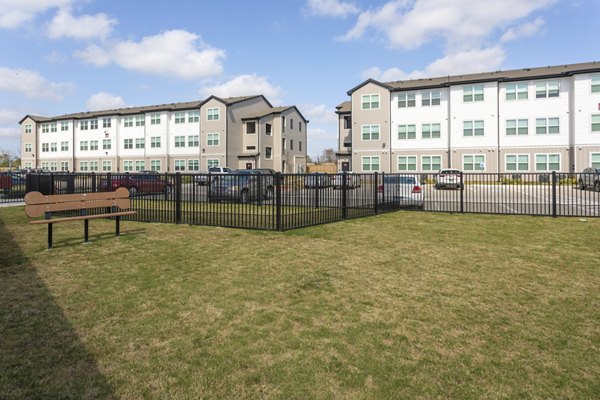 Grassy area with a bench and fenced section surrounded by luxury apartments