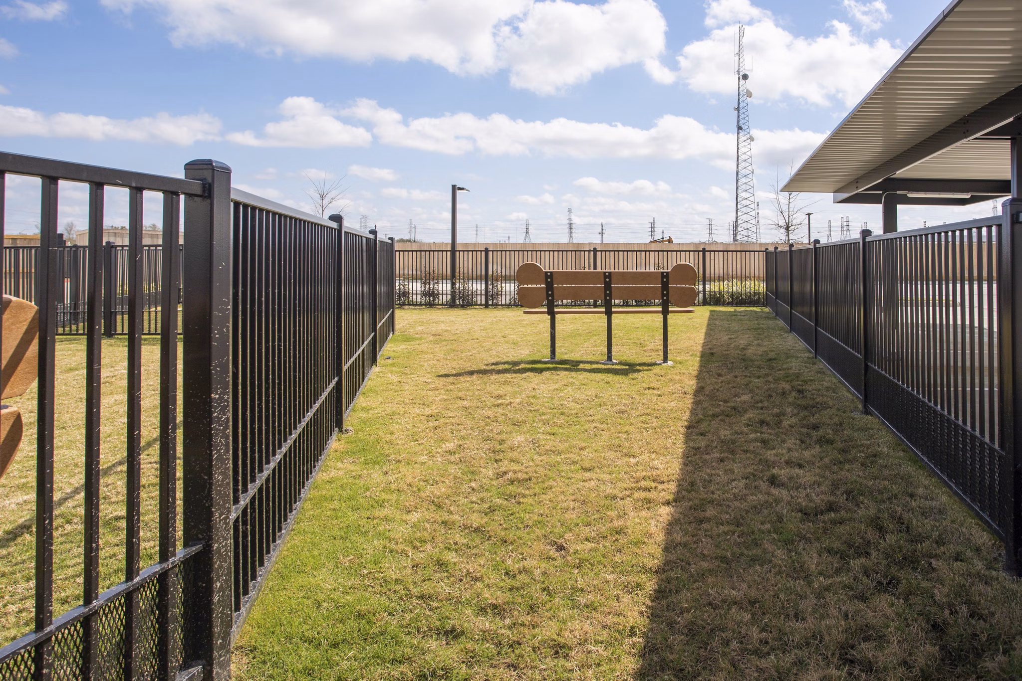 Fenced grassy area with a bench and a shaded structure near luxury apartments