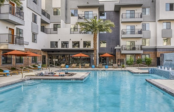 Outdoor pool area at 601 PAX Apartments with lush greenery and modern lounge chairs, offering a tranquil retreat in urban surroundings