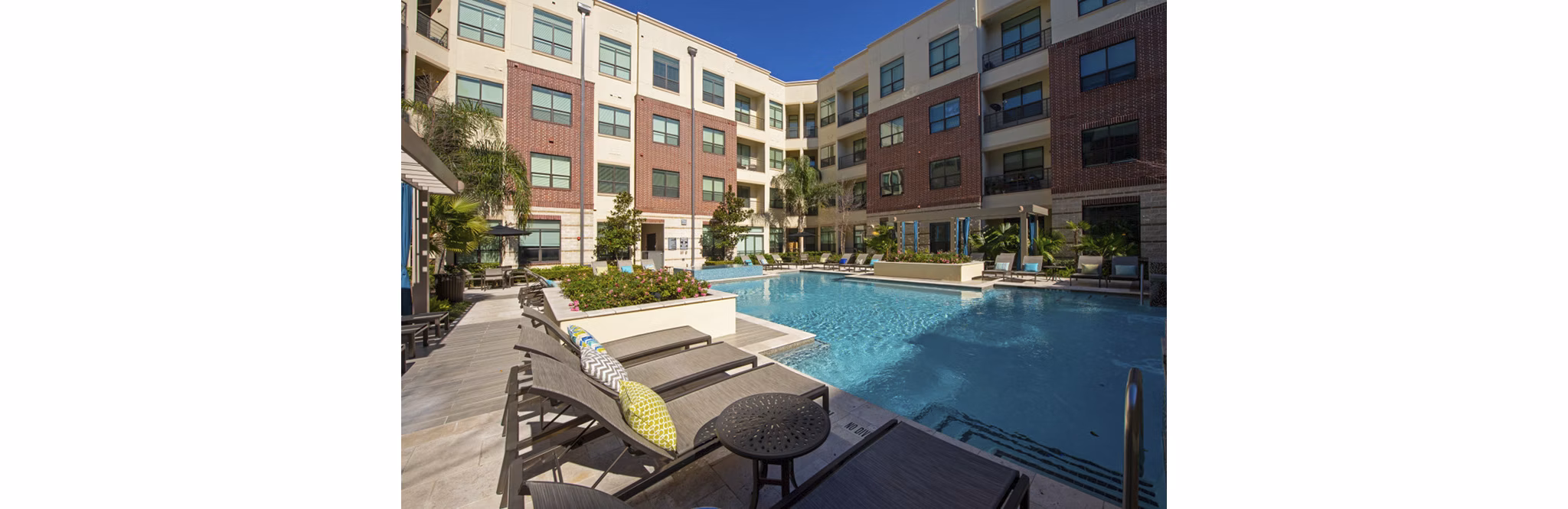Infinity-edge pool at Millennium High Street Apartments with lounge seating and lush landscaping