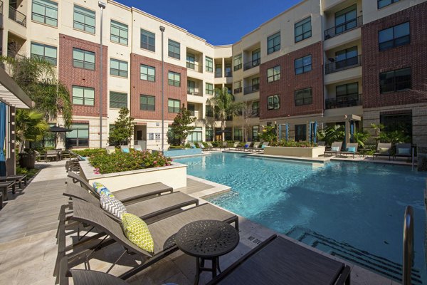 Infinity-edge pool at Millennium High Street Apartments with lounge seating and lush landscaping