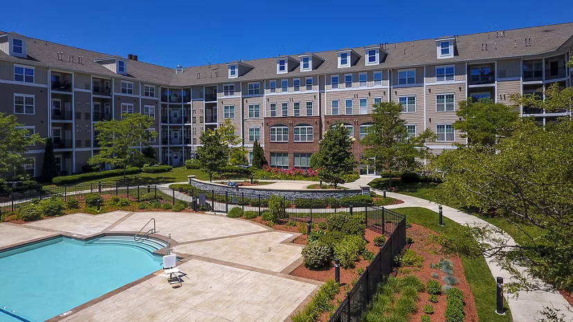 Swimming pool area with red Adirondack chairs and a modern apartment building in the backdrop