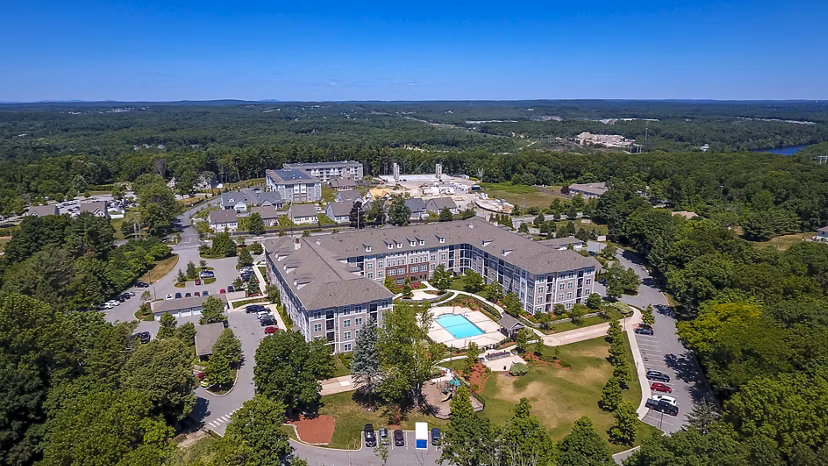 Aerial view of a luxury apartment complex featuring multiple buildings and a central pool surrounded by lush greenery