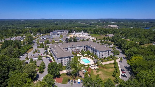 Aerial view of a luxury apartment complex featuring multiple buildings and a central pool surrounded by lush greenery
