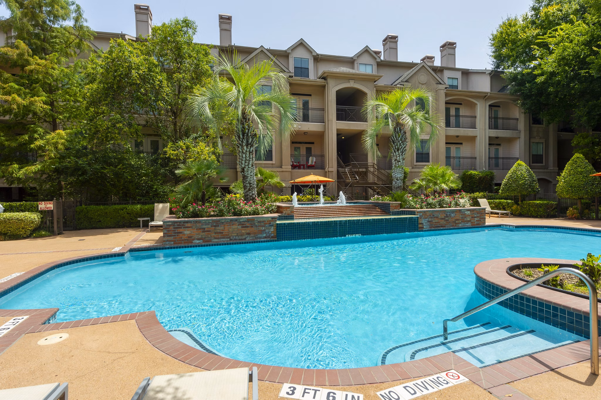 Luxurious swimming pool at The Post Oak at Woodway Apartments with lounge chairs and lush landscaping