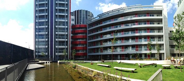 Exterior shot of a contemporary apartment complex with curved balconies, a landscaped garden, and a scenic water feature.