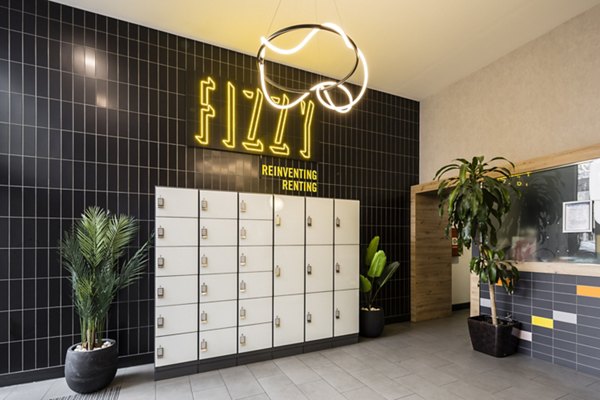 Chic community lounge area featuring lockers, greenery, and a vibrant sign reading 'Fizzy' against a black tiled wall.