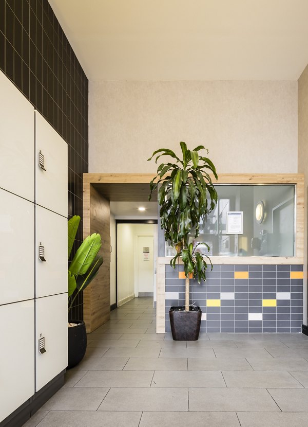 Stylish building lobby with tiled floors, a plant display, and a modern reception desk in a well-lit area.