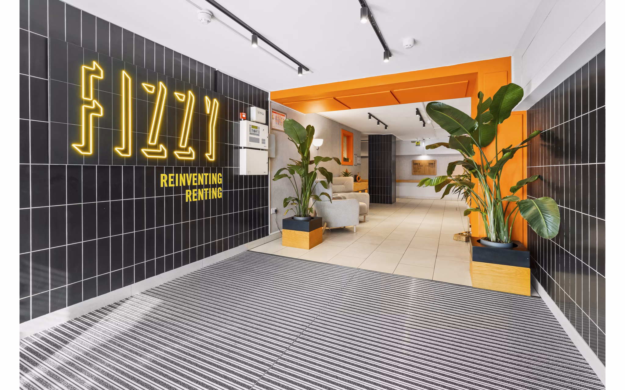 Lobby entrance of Fizzy Epsom with bold 'Fizzy' branding, sleek tiled walls, and lush greenery.