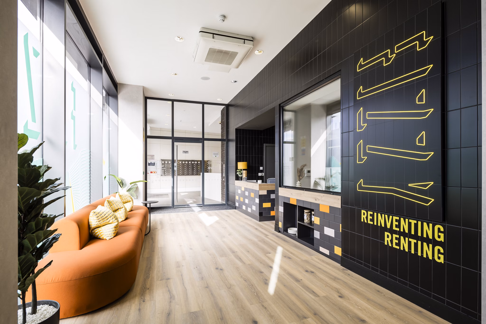 Bright communal area with contemporary furniture, a 'Reinventing Renting' neon sign, and a relaxed atmosphere.