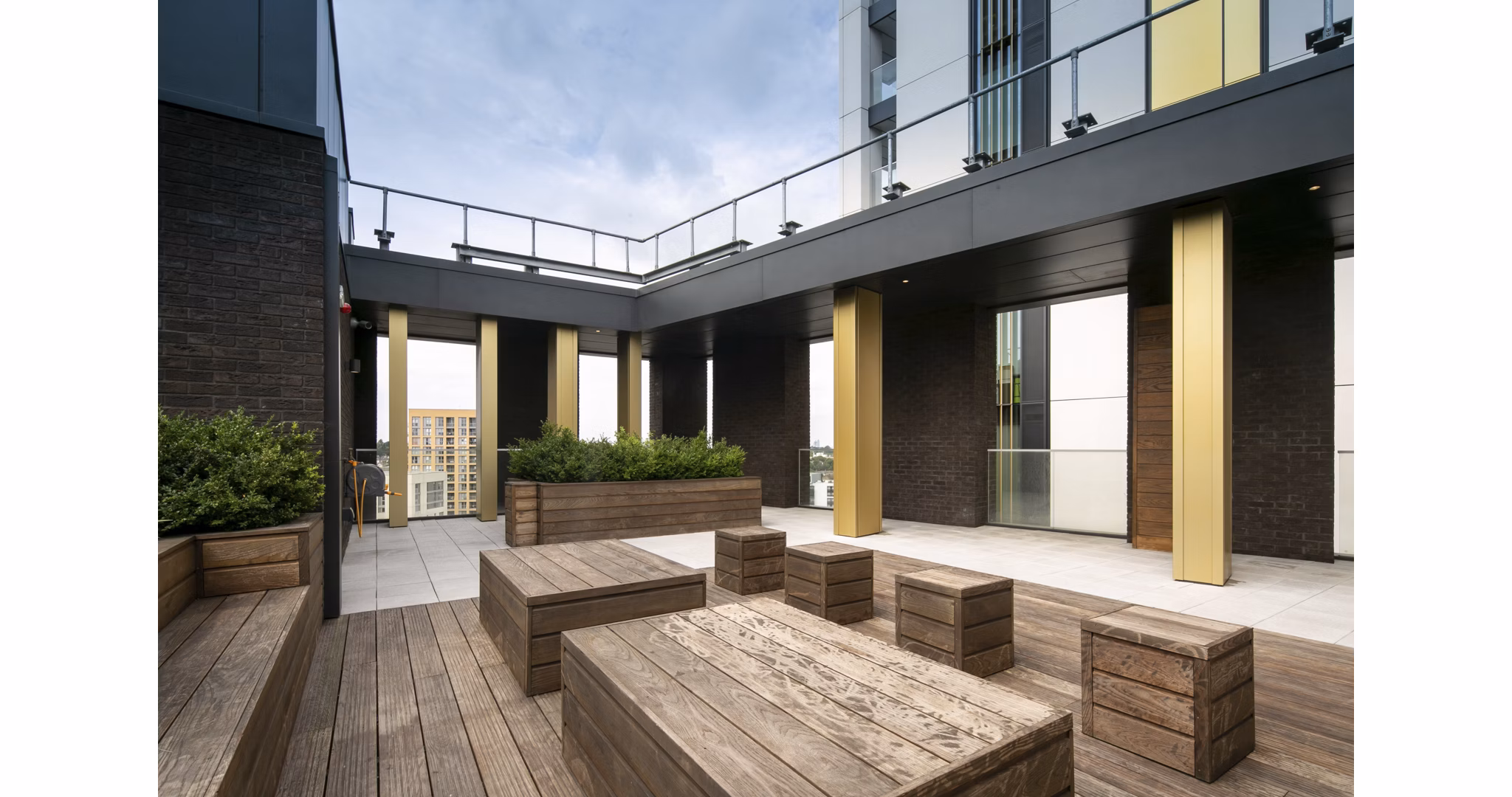 Spacious outdoor patio area at Fizzy Lewisham with wooden seating, planters, and a modern architectural design.
