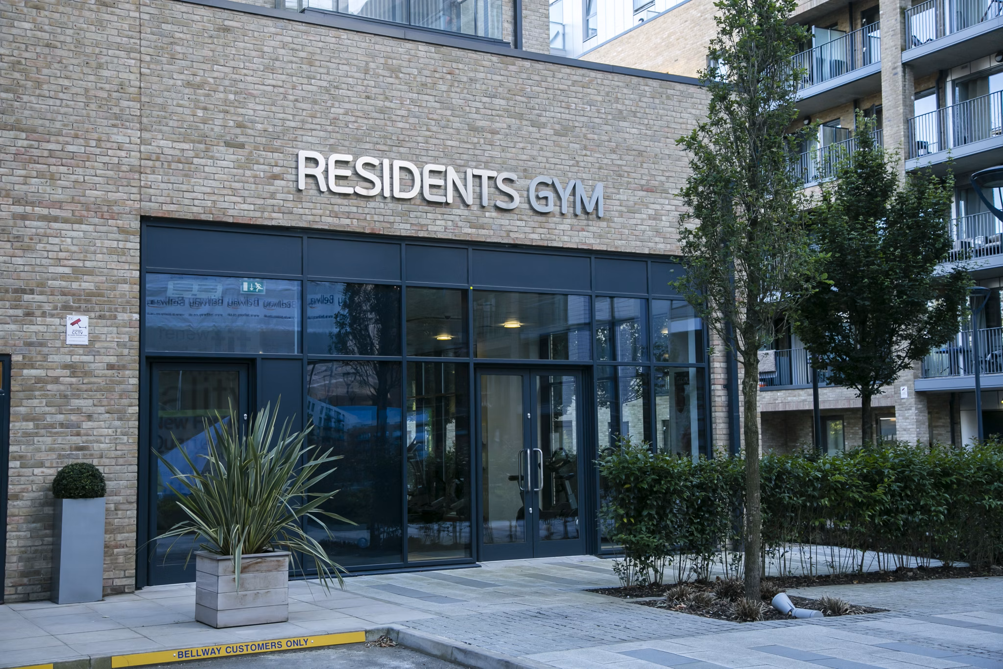 Exterior view of Fizzy Poplar's Residents’ Gym entrance surrounded by greenery and modern architecture
