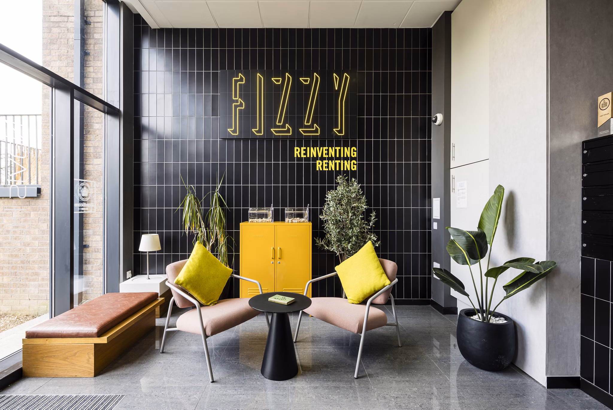 Community lounge at Fizzy Poplar with yellow chairs, a modern 'Fizzy' sign, and inviting decor.