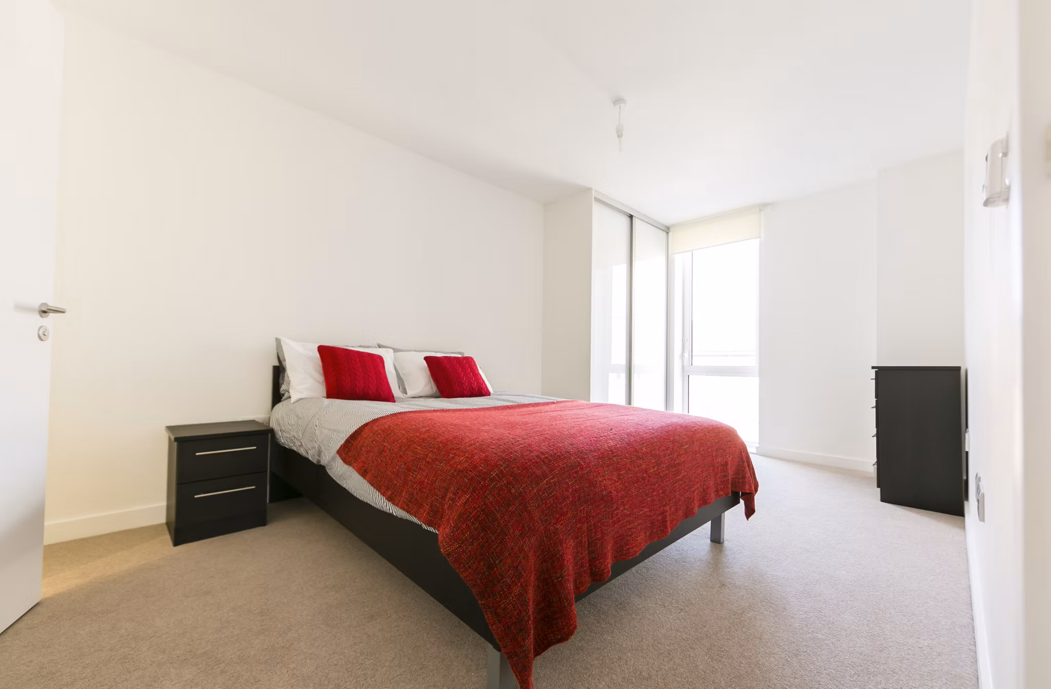 Bright and minimalist bedroom at Fizzy Stepney Green with a red blanket, modern furniture, and ample natural light.